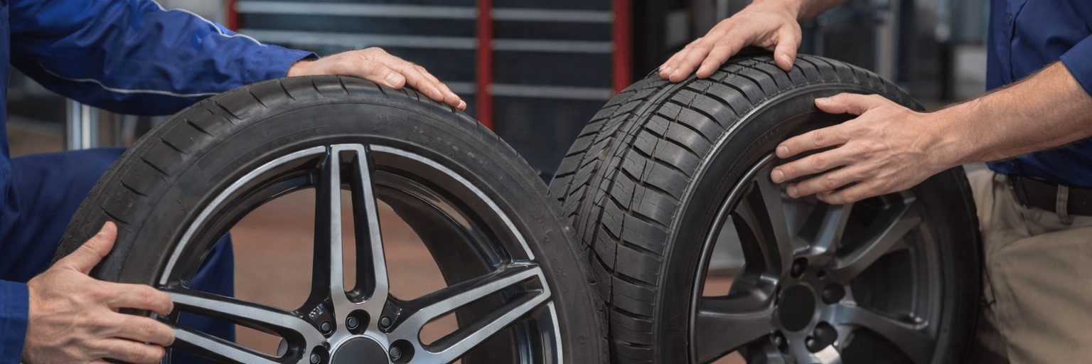 Zwei Mechaniker präsentieren und vergleichen Autoreifen und Felgen in einer Werkstatt zur professionellen Rad- und Reifenberatung